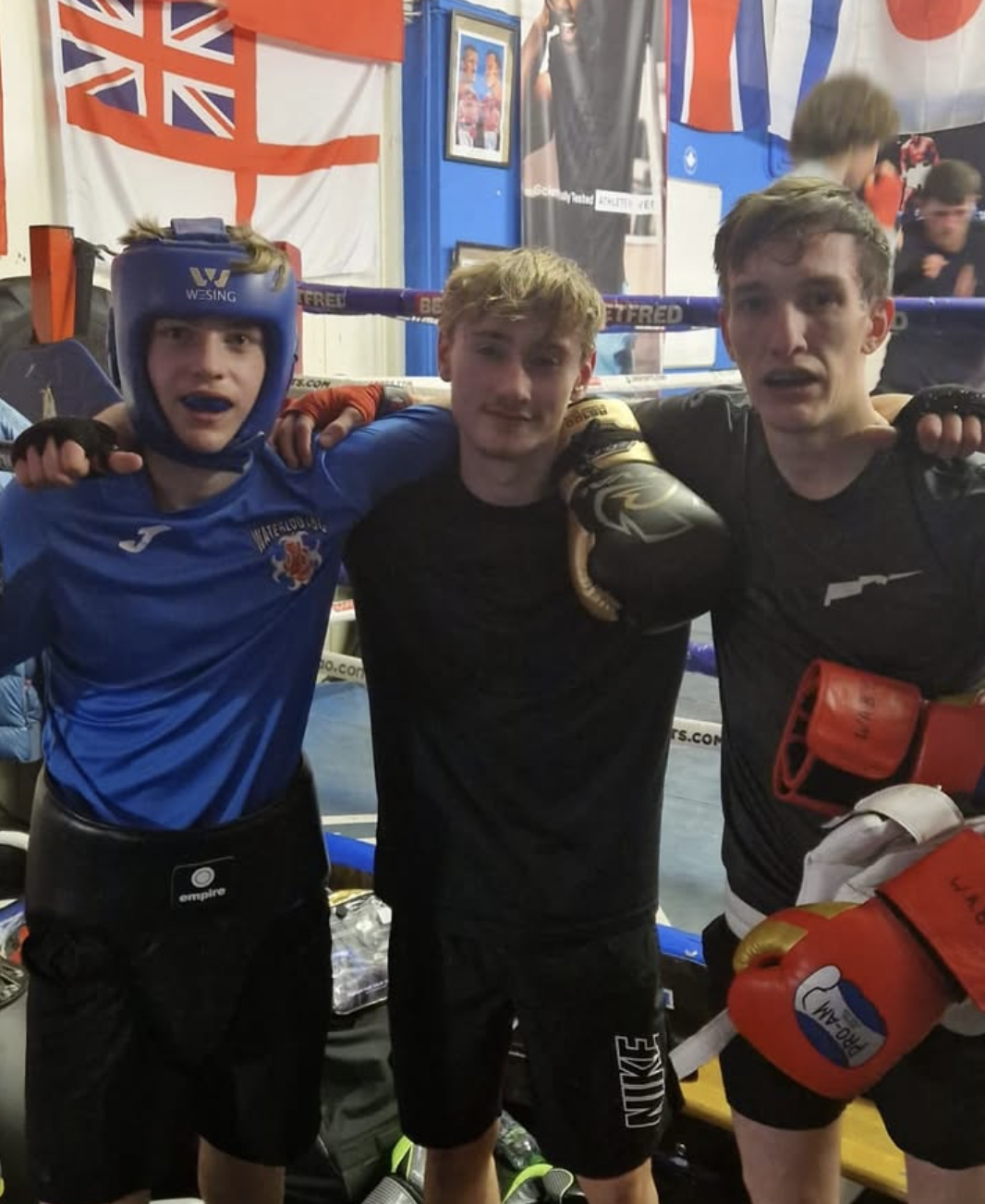 Three young Waterloo ABC fighters at a competition with flags in the background
